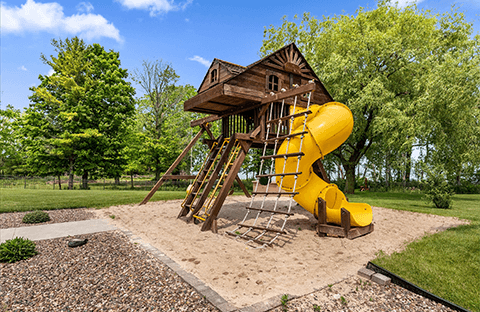 Outdoor playground area for kids at Mansion on the Lake in Newton, WI, surrounded by natural greenery with seating for parents