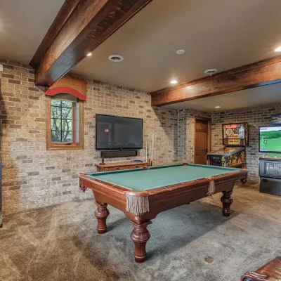 Downstairs game room at Mansion on the Lake with pool table, dartboard, TV, Cyclone, Golden Tee arcade games, and comfortable seating